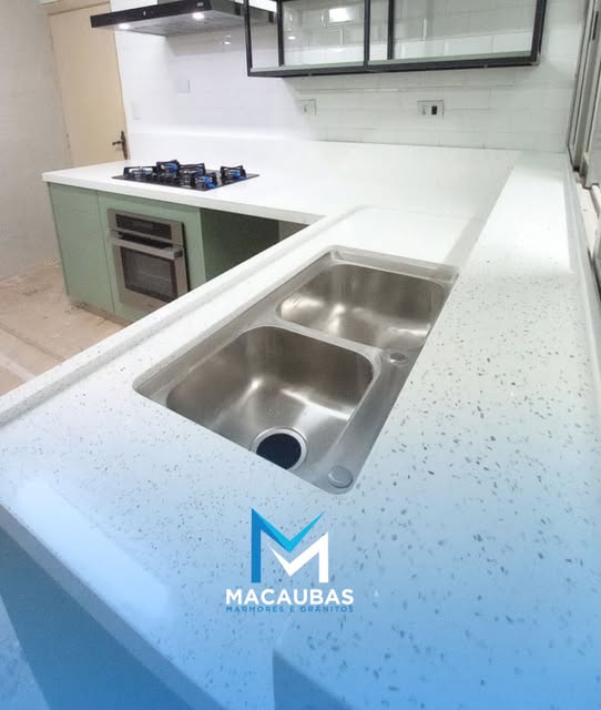 Ilha de cozinha em pedra clara com cuba dupla e cooktop ao fundo